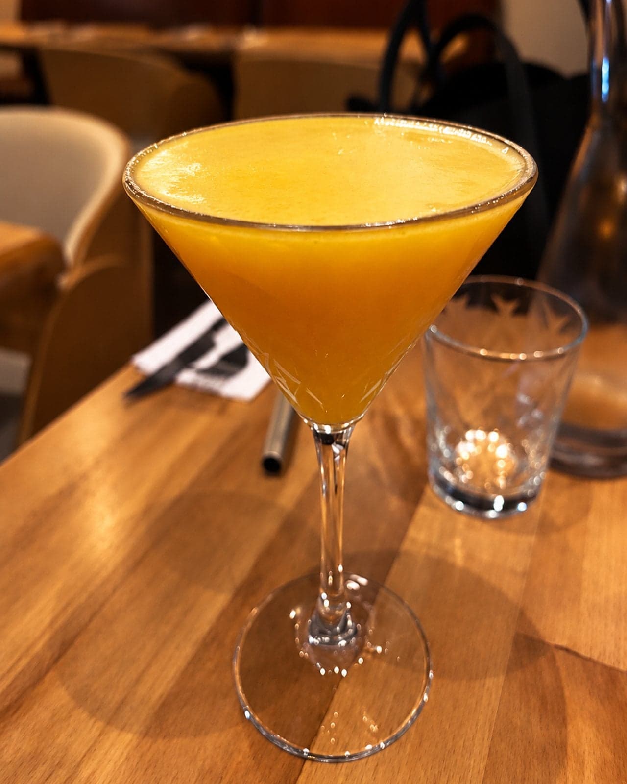 Un cocktail jaune mangue dans un verre à martini, sur une table en bois clair